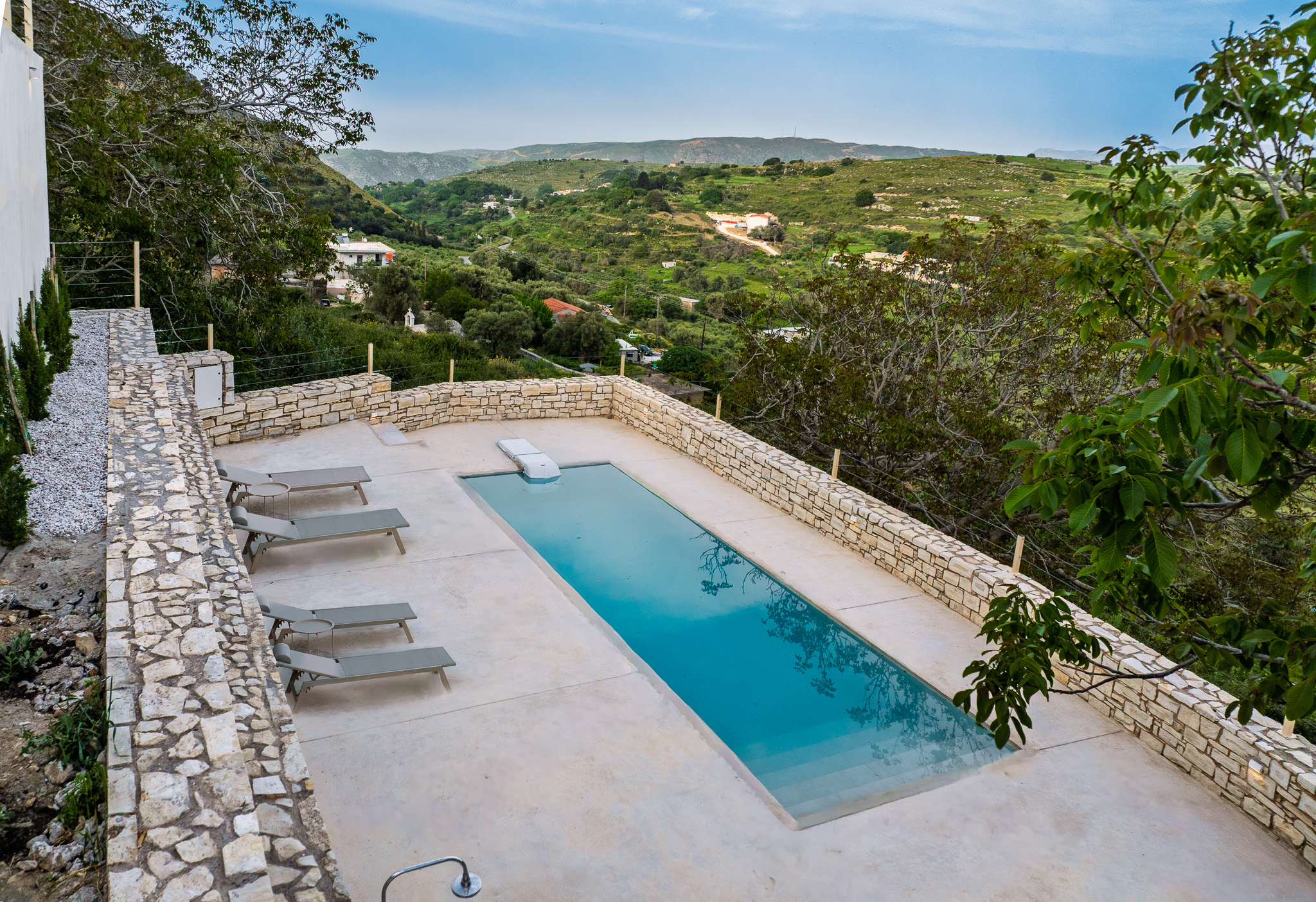 Pool with loungers, stone wall, trees, and valley view